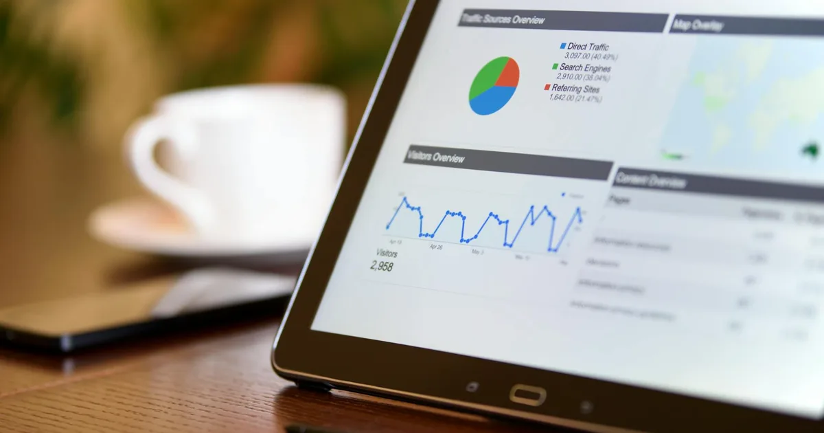 Close-up of a tablet displaying analytics charts on a wooden office desk, alongside a smartphone and coffee cup.