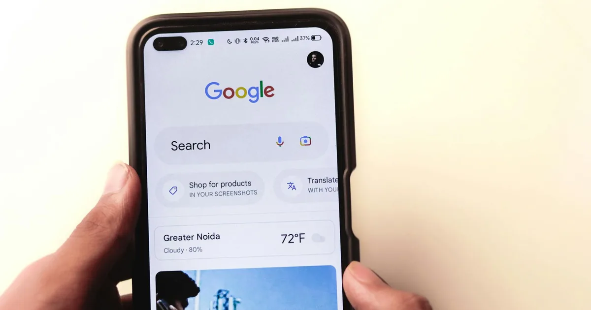 A close-up of a hand holding a smartphone with Google search displayed on the screen.