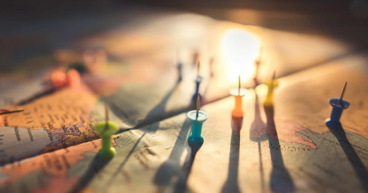 A close-up view of colorful push pins casting shadows on a world map during sunset, highlighting global travel.