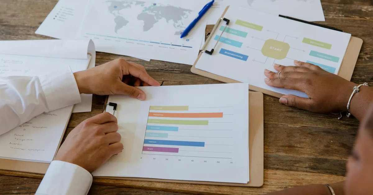 Top view of colleagues discussing charts and graphs on a wooden table during a business meeting.