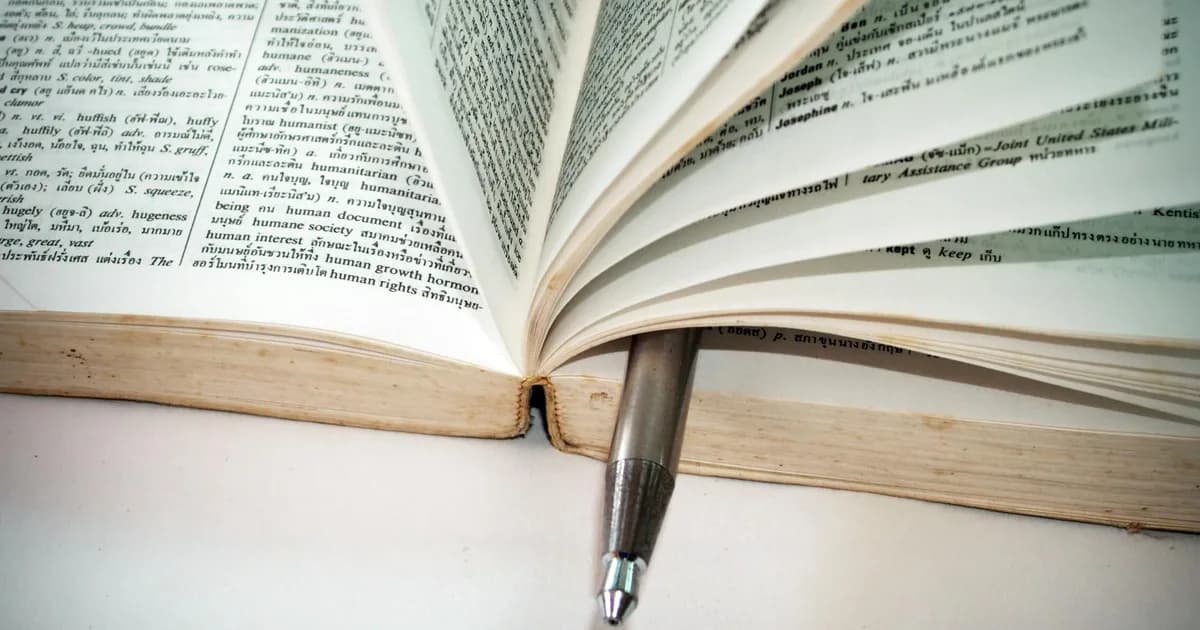 A close-up of an open dictionary with a pen separating the pages for convenient reference.