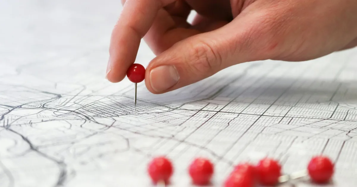 Close-up of a hand placing a red pin on a map indicating geographic location pinning.