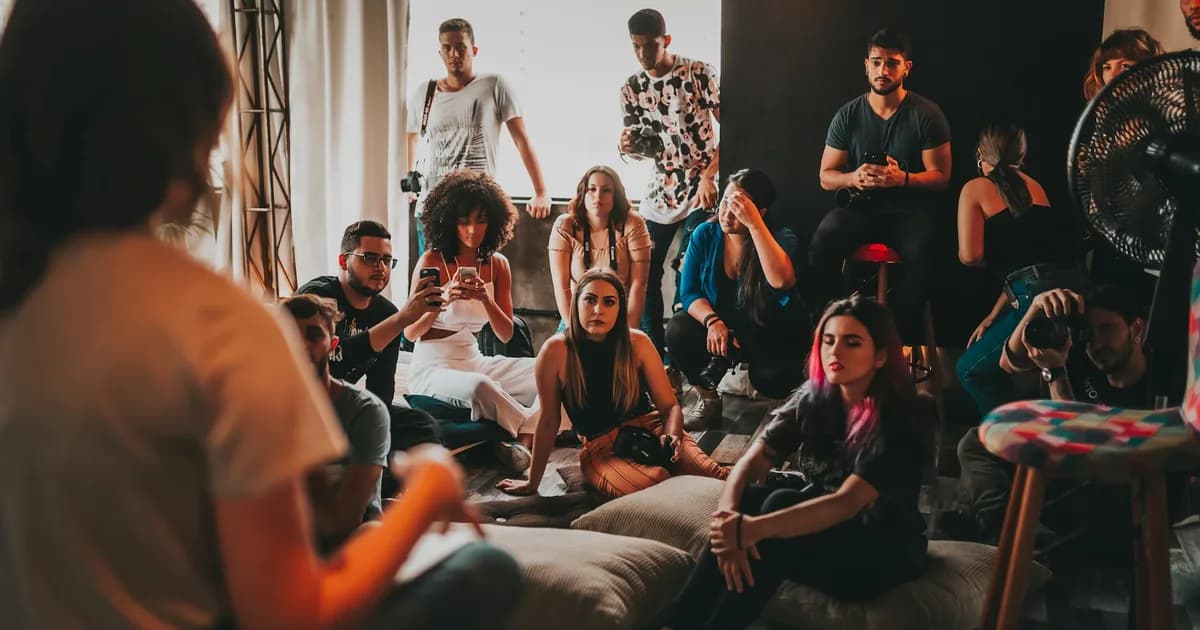 Group of attentive young multiracial community members in casual outfits meeting in modern studio and listening to female speaker sitting on mat