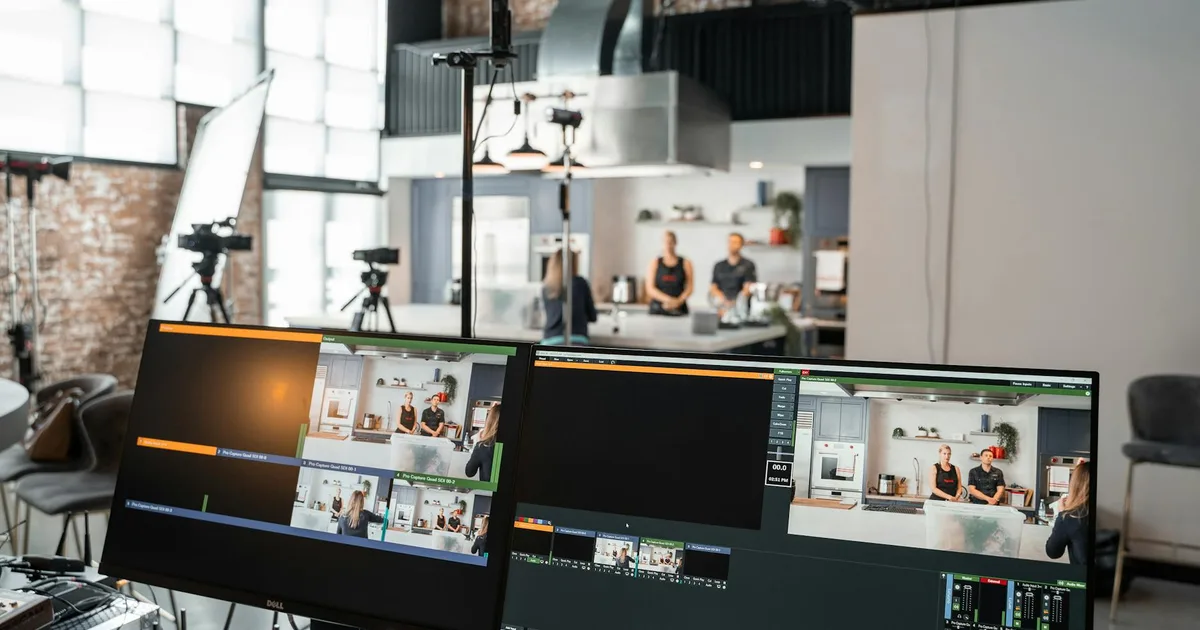 A dynamic setup in a video production studio with two monitors and a kitchen setting.