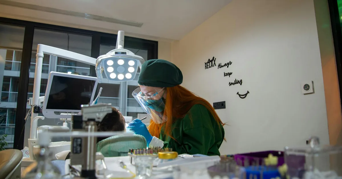 A female dentist in green scrubs performing a dental procedure on a patient in a modern clinic.