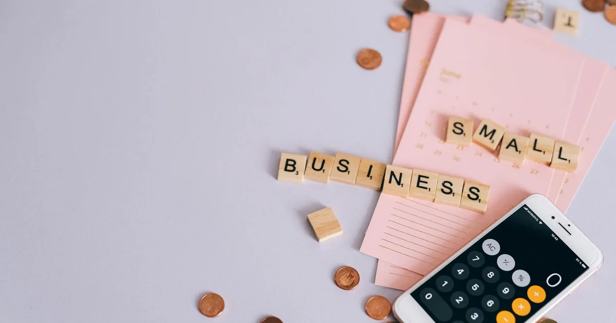 Flat lay of a small business planning scene with coins, smartphone calculator, and letter tiles.