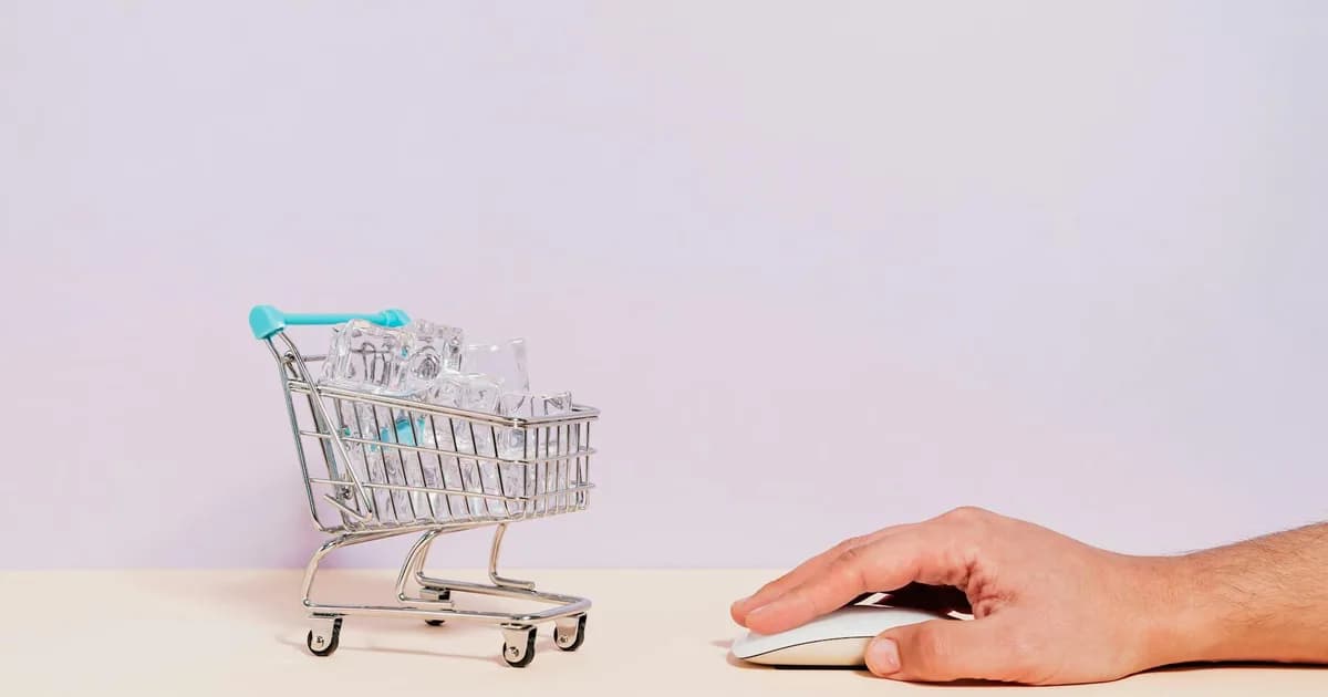 Conceptual image of a hand on a mouse next to a miniature shopping cart filled with ice cubes, symbolizing online shopping.