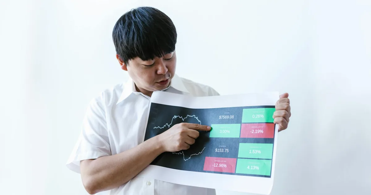 Asian businessman in white shirt presenting cryptocurrency market data on chart.