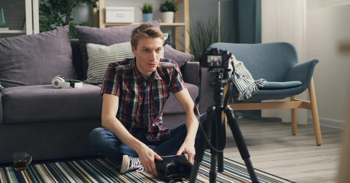 Young man sitting on the floor filming a vlog in a cozy living room with camera and tripod.